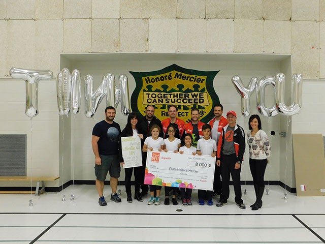 people holding a cheque with grey baloons spelling thank you in the background