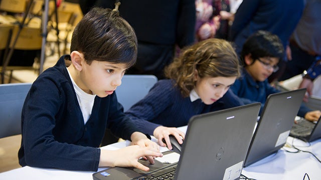 Elementary students intently coding on laptops