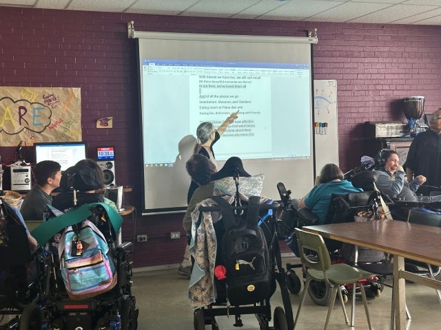 C.A.R.E. clients in wheelchairs pictured working on a creative project in a classroom.