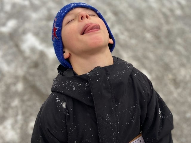 A young student turns his head up to the sky and catches snowflakes on his tounge.