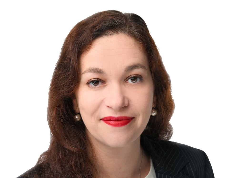 An official headshot of Elisabeth Prass. She has long brown hair and is wearing a white shurt and dark blazer.