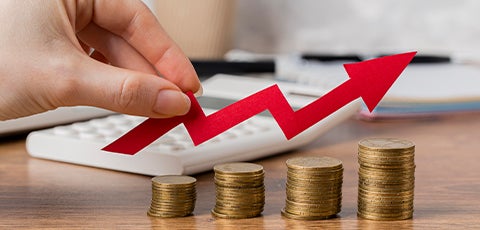 Mano caucásica sosteniendo una flecha con dirección positiva, sobre montículos de monedas que están ordenados de menor a mayor cantidad.