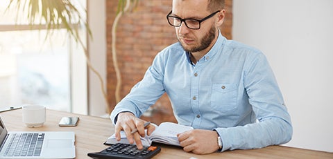 Hombre con camisa celeste con un cuaderno de anotaciones y una calculadora, calculando la igv que deberá pagar.