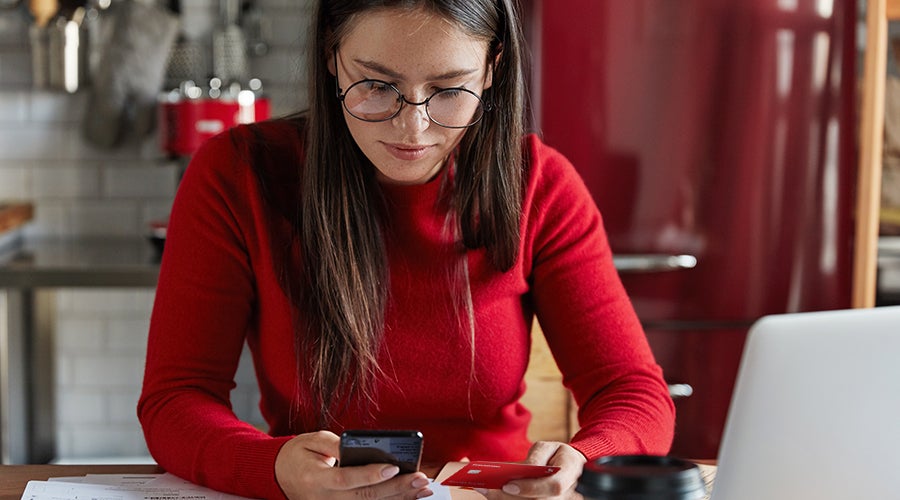 mujer en plano medio vestida de rojo viendo opciones de pr&eacute;stamos bancarios con tarjeta en mano