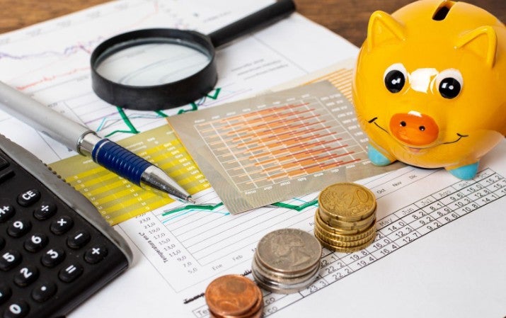 Monedas, un lapicero, una calculadora, un chanchito de ahorro, una lupa u hojas con datos numéricos de cuentas sobre la TCEA en un préstamo.