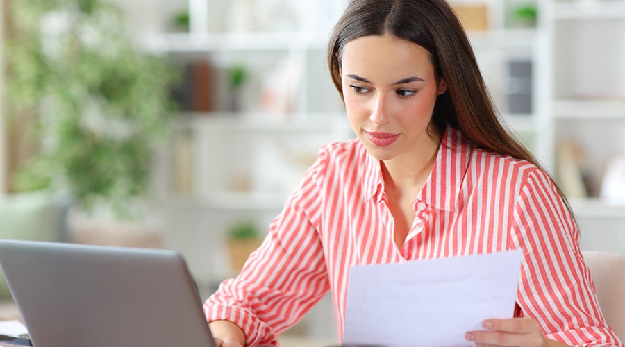 Mujer revisando un documento financiero frente a su laptop para evaluar un pr&eacute;stamo
