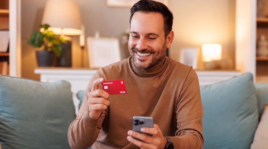 Hombre sonriente con su tarjeta Scotiabank y su celular tras recibir dinero del extranjero