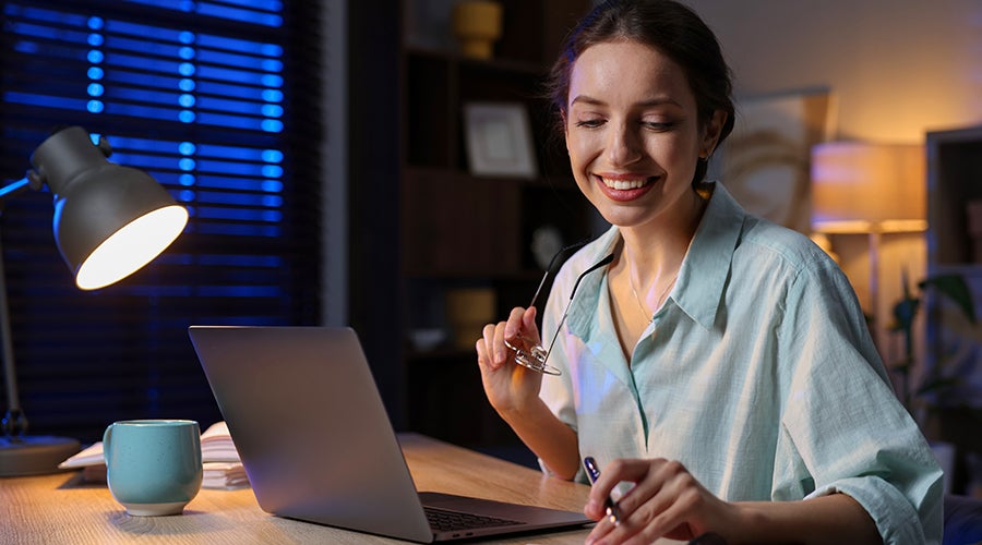 Mujer sonriente revisando sus finanzas en la laptop por la noche
