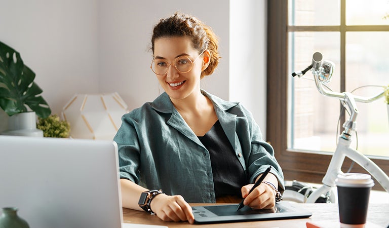 Mujer trabajando desde casa con su laptop y una tableta gráfica
