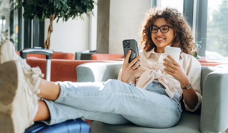 Mujer en la sala de espera del aeropuerto revisando su celular junto a su maleta