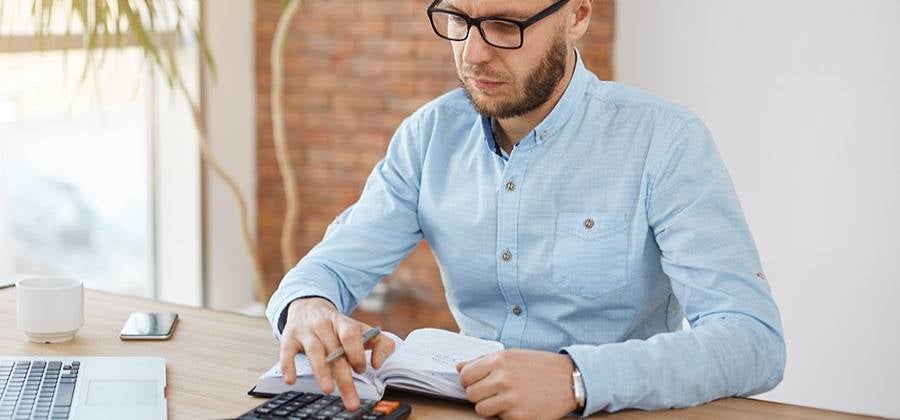 Hombre con camisa celeste con un cuaderno de anotaciones y una calculadora, calculando la igv que deberá pagar.