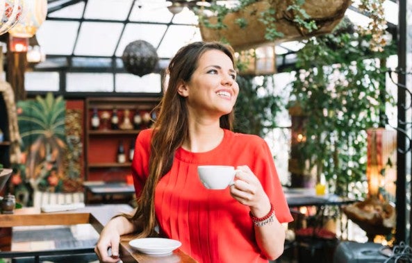 Mujer joven sonriente con la taza de caf&eacute; en caf&eacute;